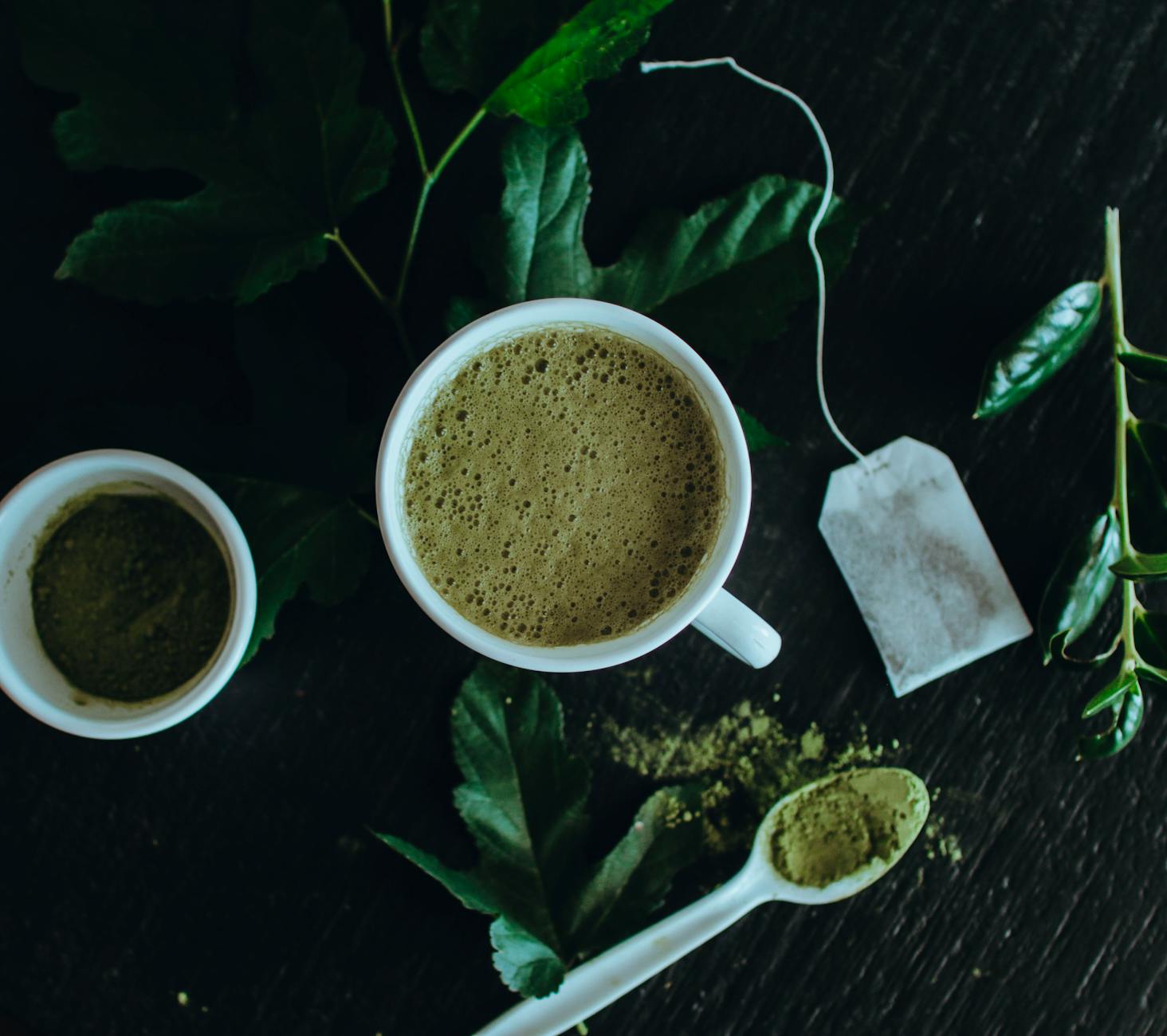 Matcha latte z proszkiem herbacianym, listkami i torebką herbaty z góry