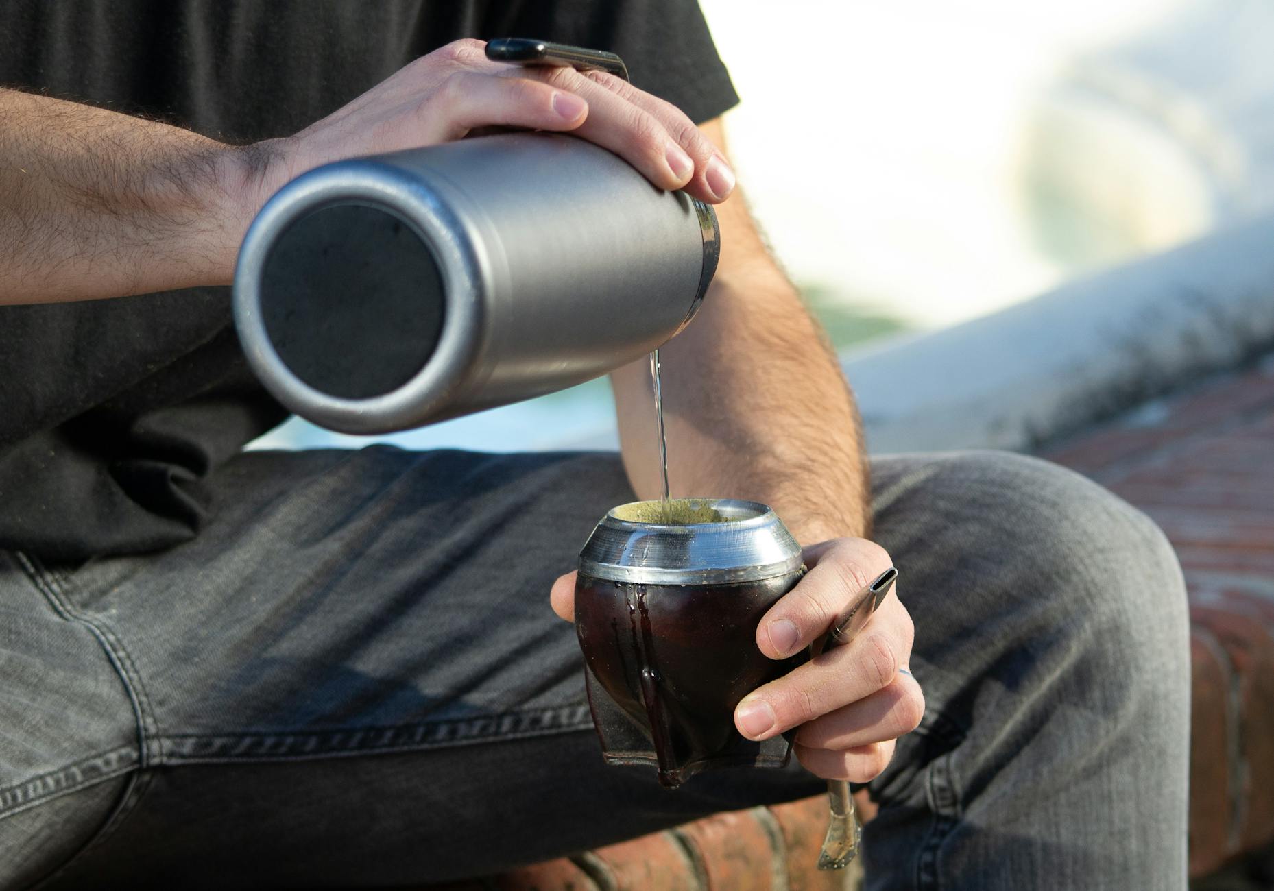 Mężczyzna na dworze nalewa gorącą wodę do tradycyjnego naczynia mate