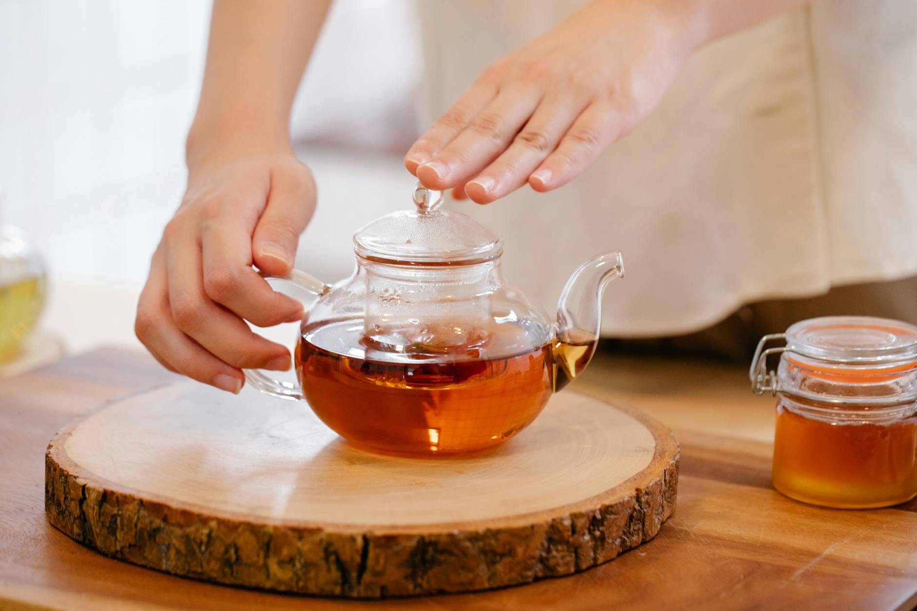 Dłonie przygotowujące herbatę rooibos w szklanym czajniku