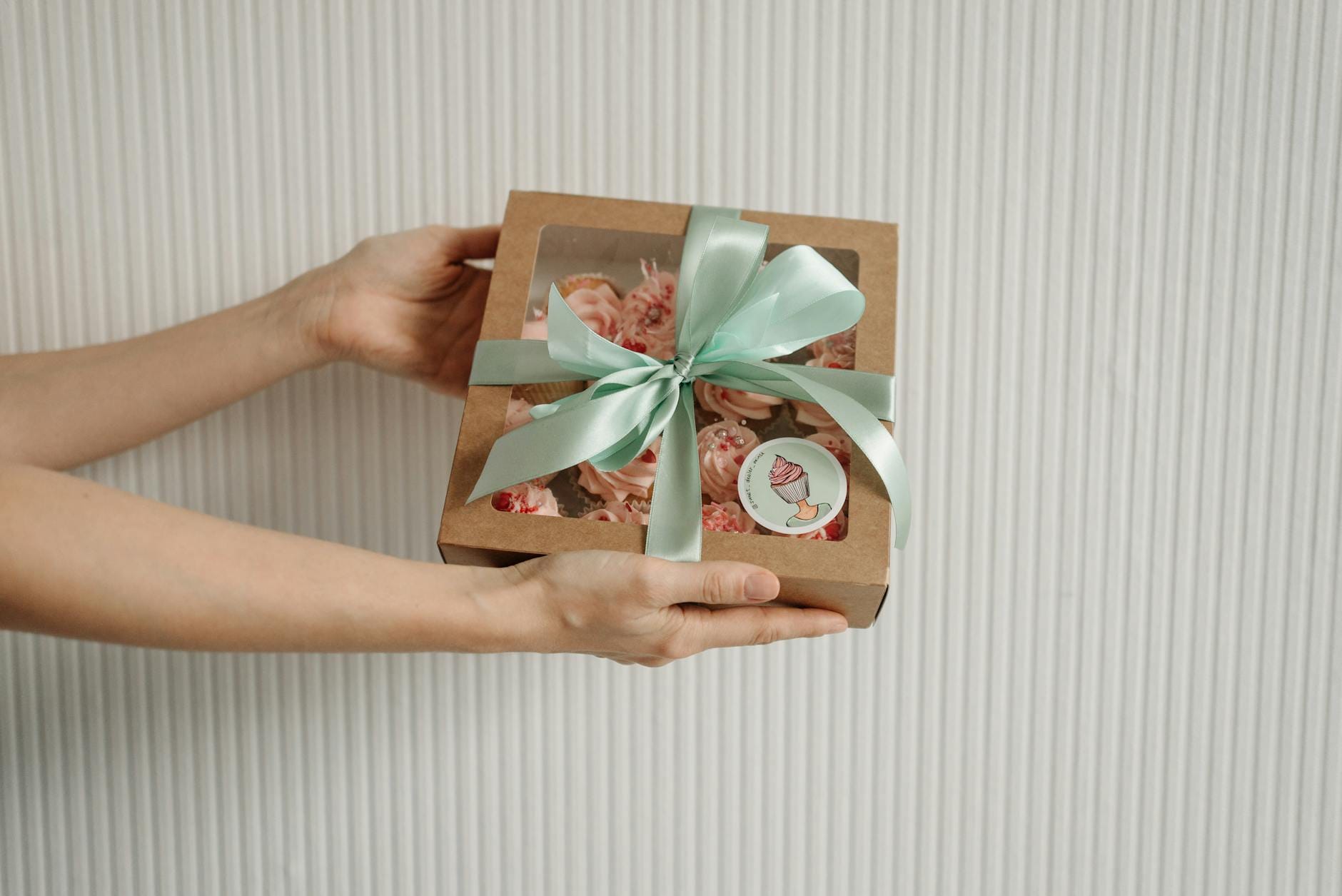 Dłonie trzymają pudełko z babeczkami przewiązane miętową wstążką