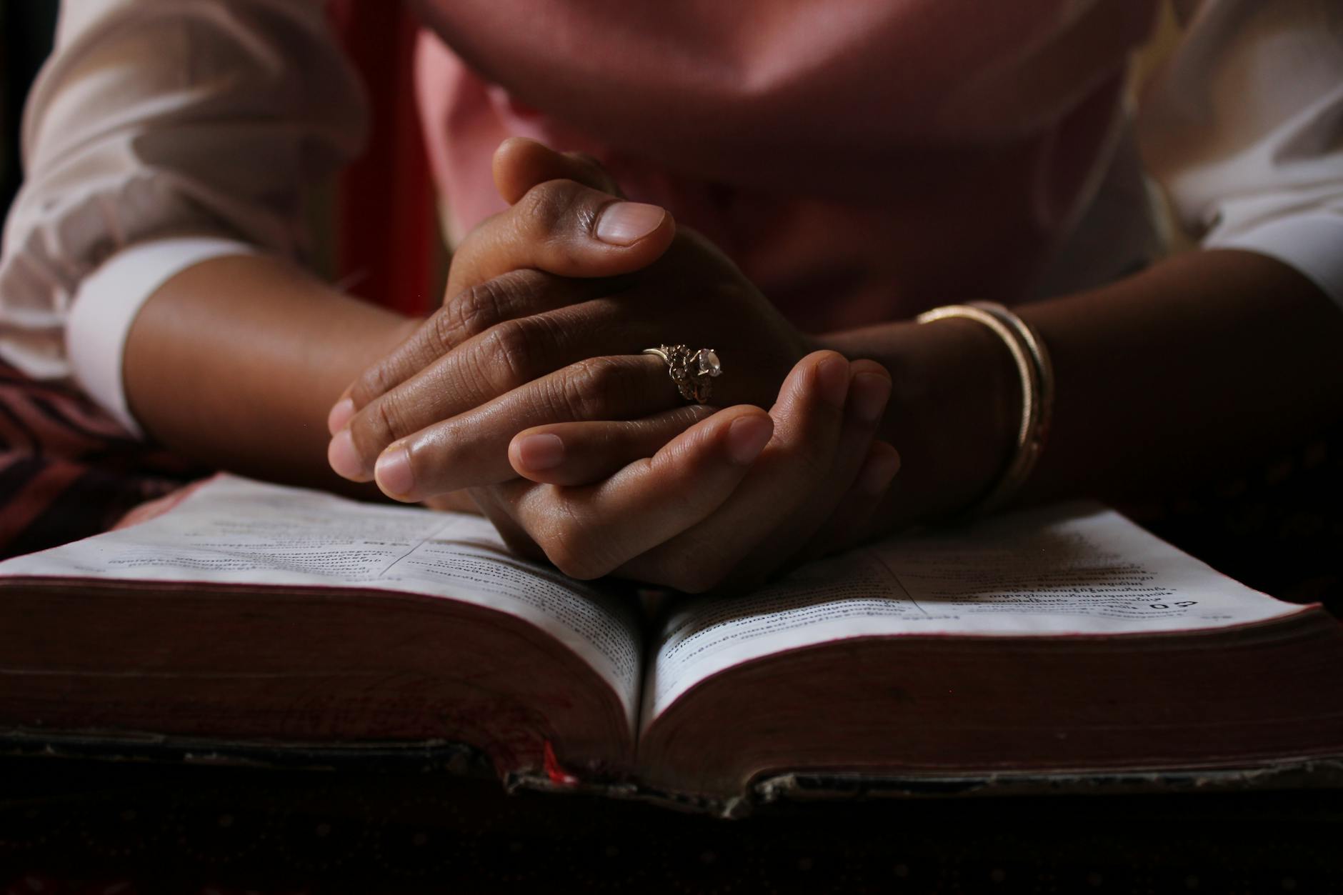 Złożone dłonie w modlitwie nad otwartą Biblią na stole