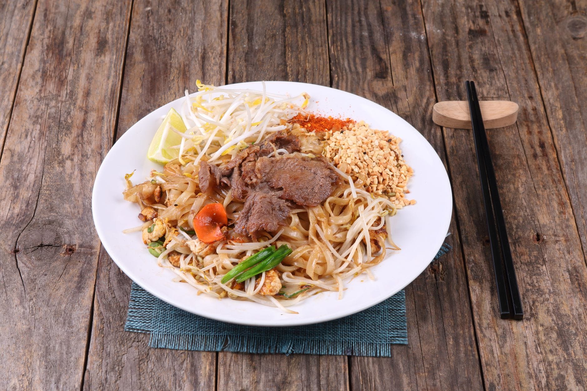 Pad thai z wołowiną, orzeszkami i warzywami podany na drewnianym stole