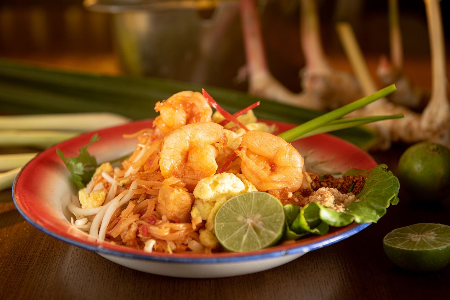 Talerz pad thai z krewetkami podany z limonką i świeżymi ziołami