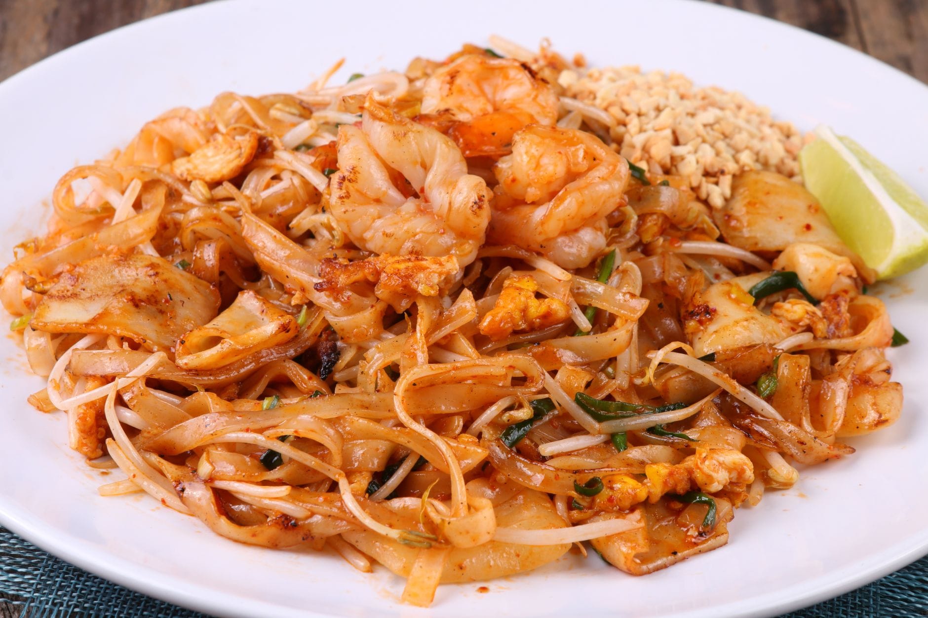 Zbliżenie na pad thai z krewetkami, limonką i orzeszkami na białym talerzu